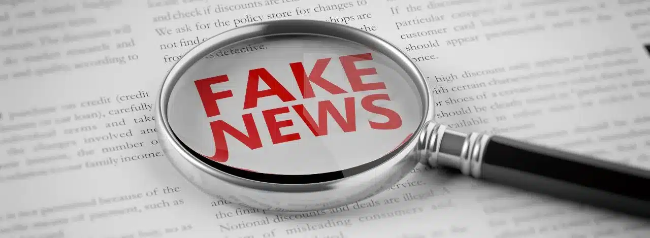 Imagem com uma lupa enfatizando a palavra Fake News em vermelho.