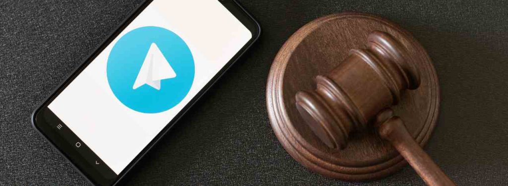 Foto de um celular com o logo do telegram, emcima de uma mesa, ao lado de um martelo da justiça, simbolizando as decisões da justiça em relação ao Telegram.