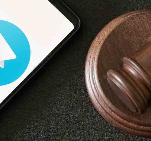 Foto de um celular com o logo do telegram, emcima de uma mesa, ao lado de um martelo da justiça, simbolizando as decisões da justiça em relação ao Telegram.